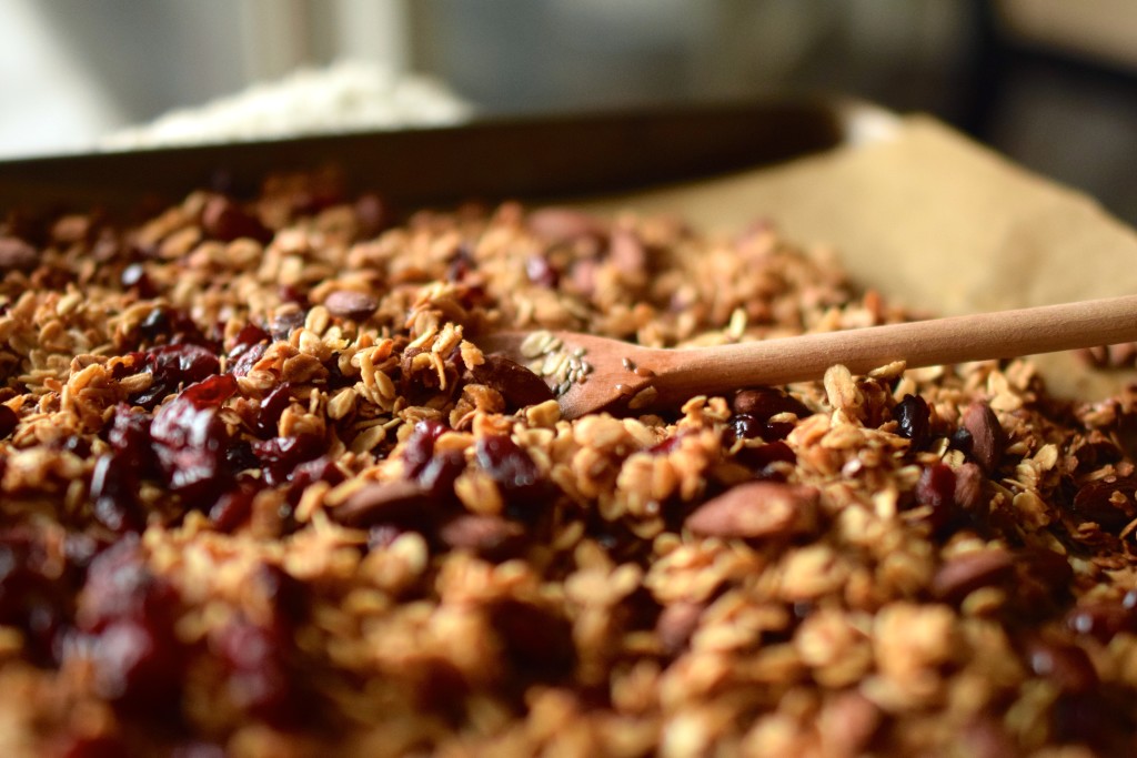 Granola with dried cranberries on a baking sheet with a wooden spoon