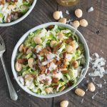 Two bowls of shaved brussels sprout salad with a carafe of dressing, shot from overhead