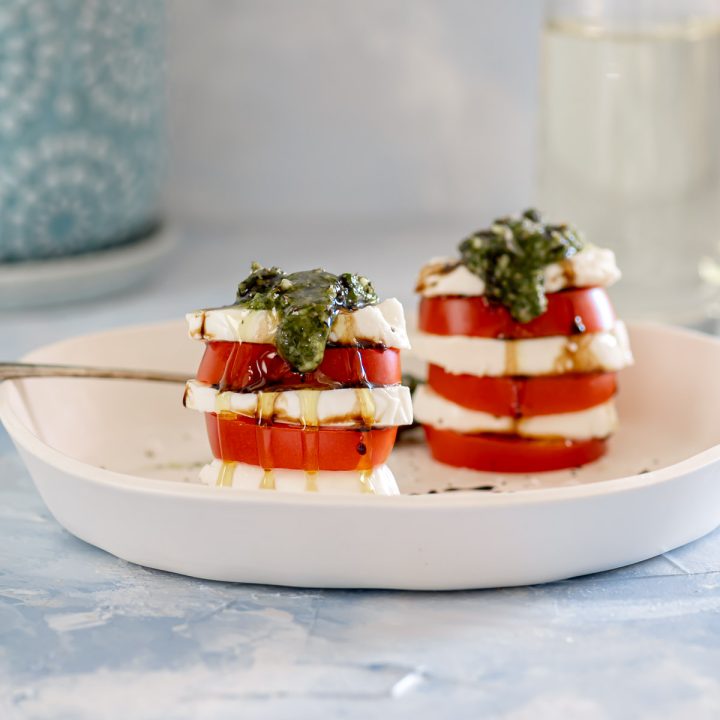 Two stacks of tomatoes and fresh mozzarella topped with pesto and balsamic glaze