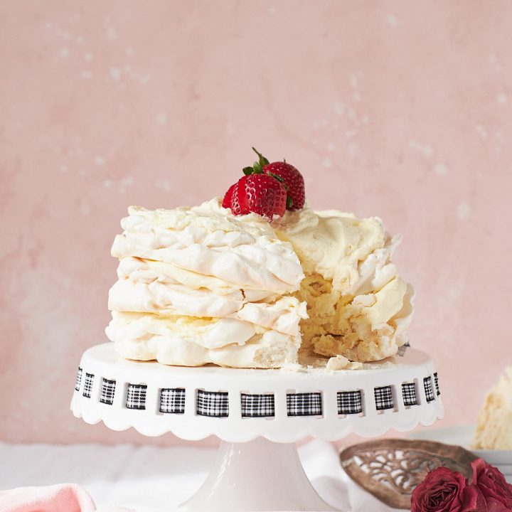 Three meringue disks stacked and topped with lemon cream on a white cake stand