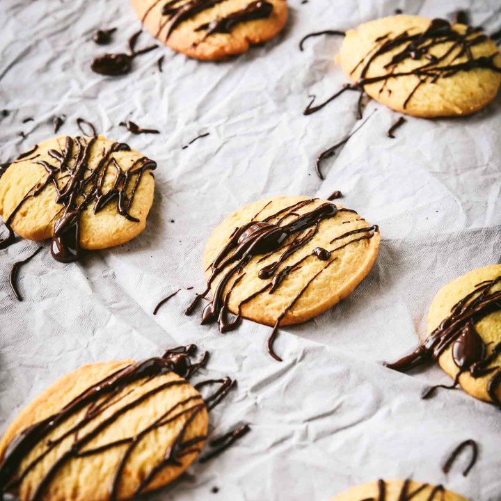 Orange crisp cookies on white parchment paper drizzled with chocolate