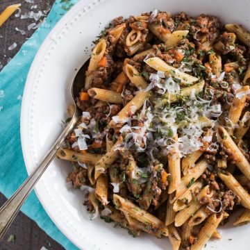 Large white pasta bowl filled with penne pasta topped with bolognese sauce