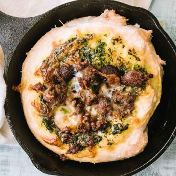Skillet pizza topped with kale pesto, sausage & mushrooms