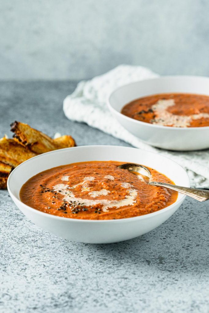 Two white soup bowls filled with tomato bisque