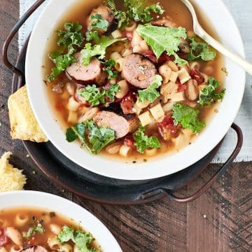 Two bowls of tomato based soup with sauage, pasta, white beans and kale