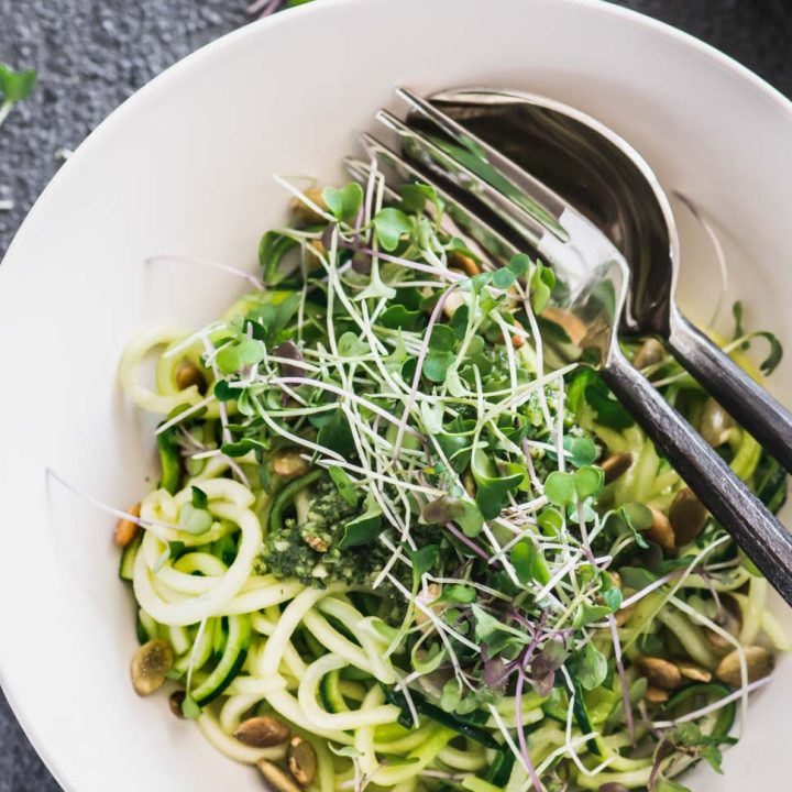 Zucchini noodles in a cream bowl topped with basil almond pesto and micro greens