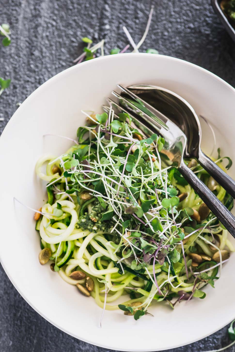 Zucchini noodles in a cream bowl topped with basil almond pesto and micro greens