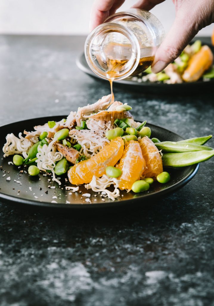 Dressing being poured over Asian Chicken Salad on a black matte plate
