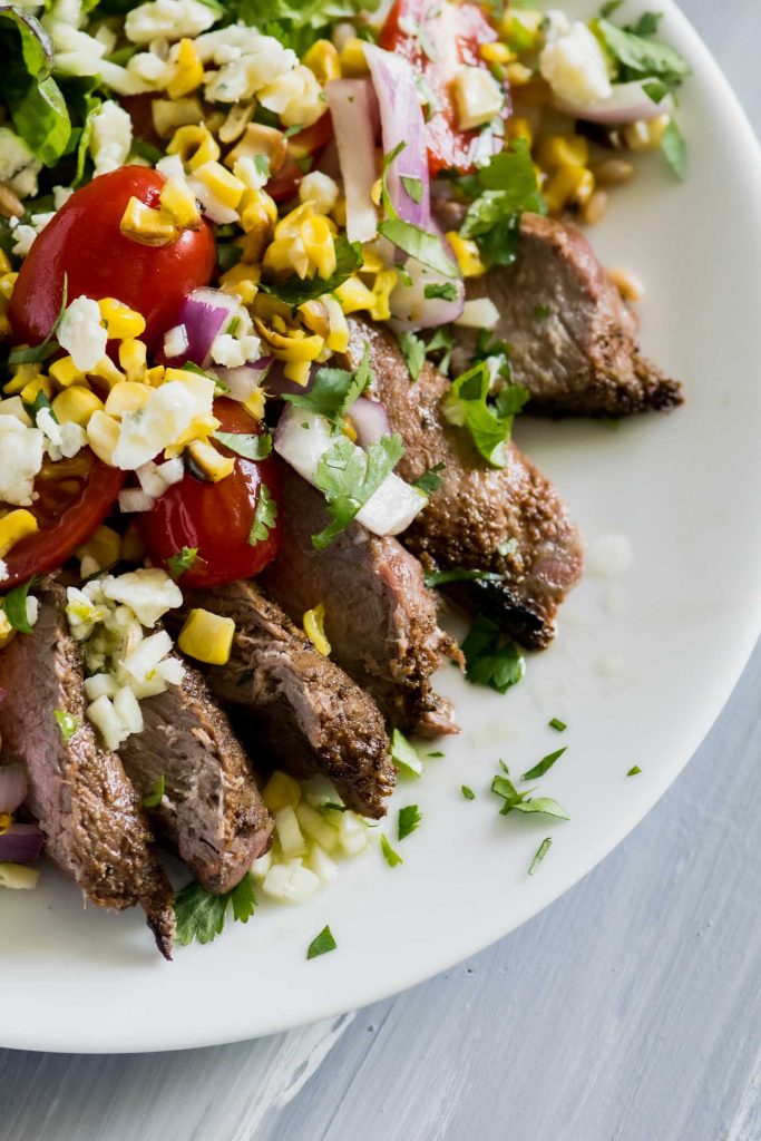 Close up of a grilled steak salad topped with grilled corn