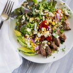 Overhead shot of salad with grilled steak, avocado slices and grape tomatoes