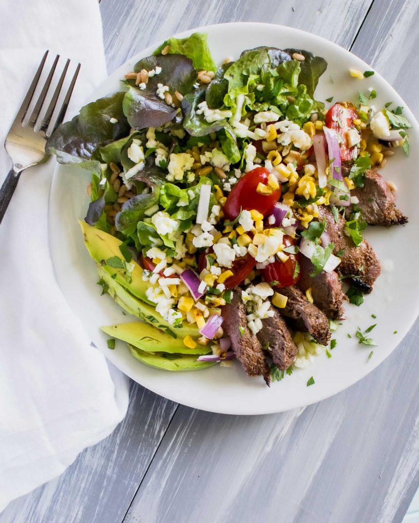 Overhead shot of salad with grilled steak, avocado slices and grape tomatoes