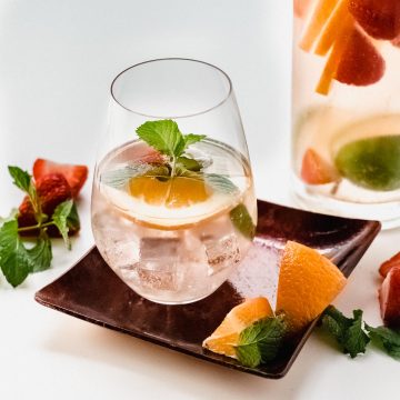 Glass of Rose Sangria on a small red dish with the pitcher in the background