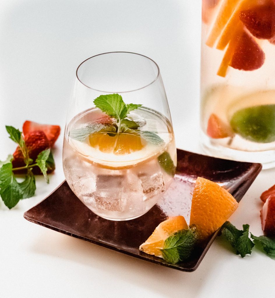 Glass of Rose Sangria on a small red dish with the pitcher in the background