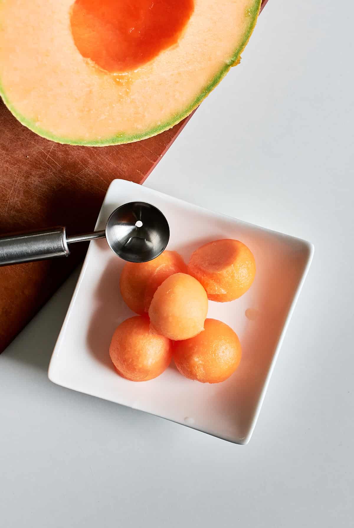 Small balls of cantaloupe in a square white dish. 