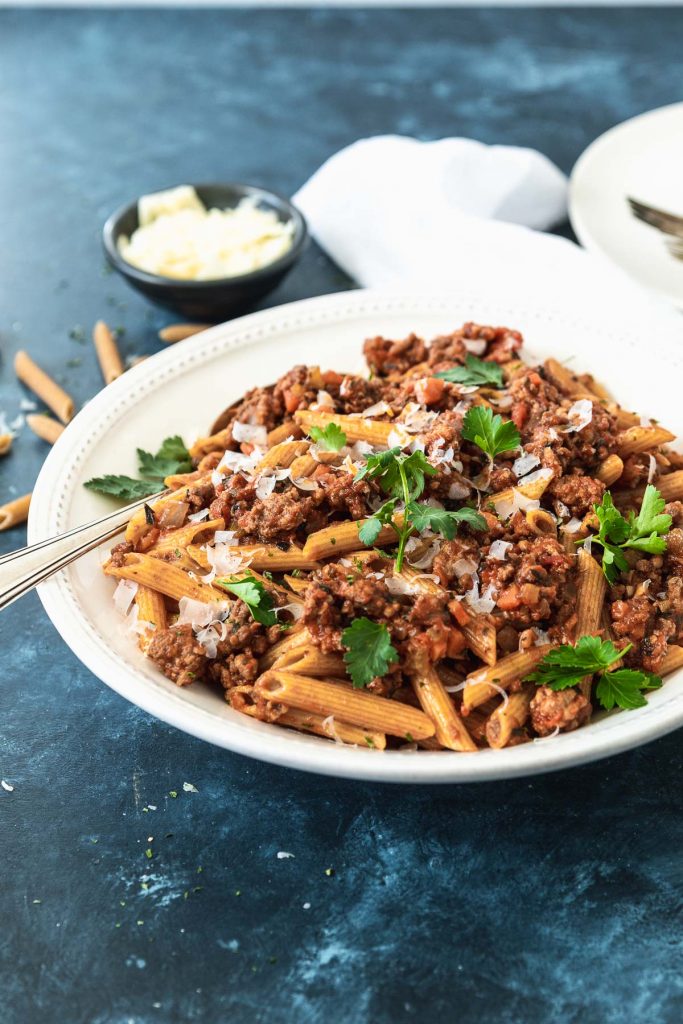 Large white pasta bowl filled with penne and bolognese sauce