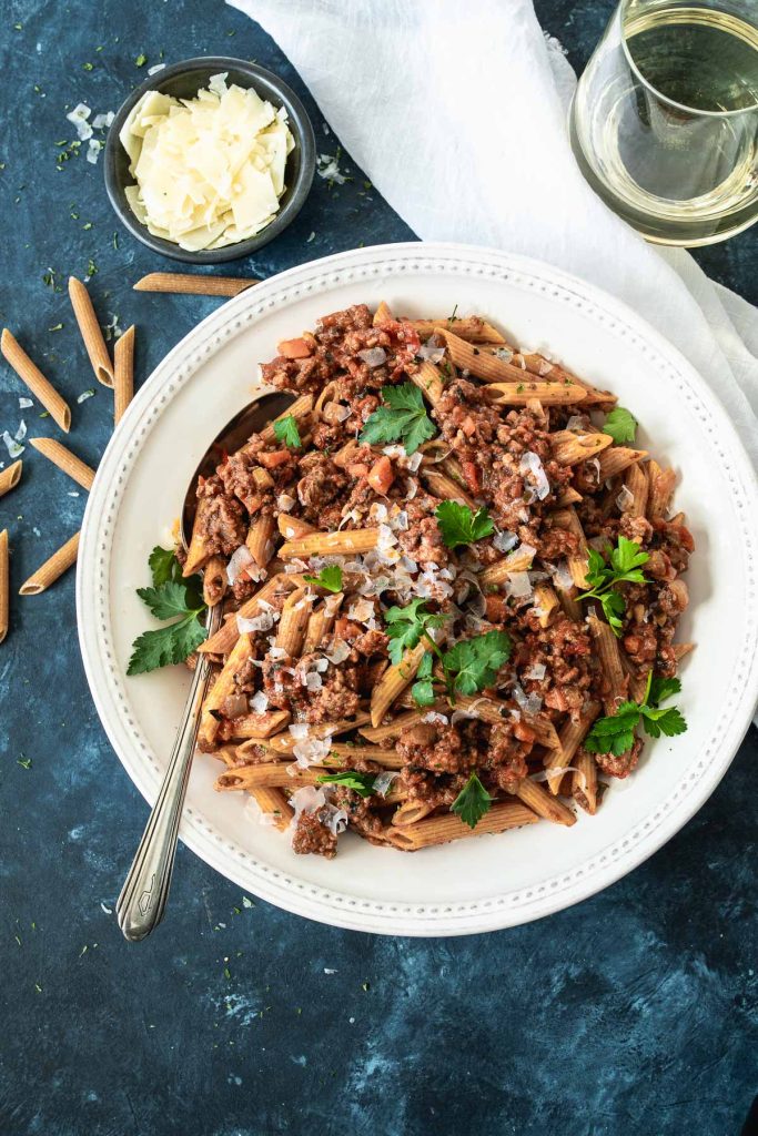 Overhead shot of a large white bowl filled with penne pasta and topped with bolognese sauce and grated cheese