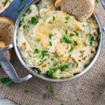 Hot Artichoke Crab Dip in a mini gratin dish with crostini for dipping.