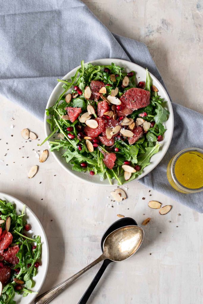 Bowl of arugula topped with grapefruit segments, pomegranate arils and toasted almonds