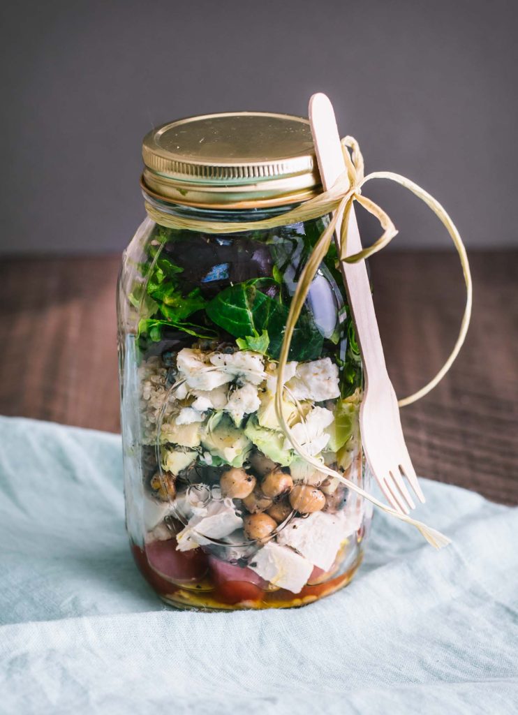Layered salad in a mason jar with a picnic fork attached by a piece of string