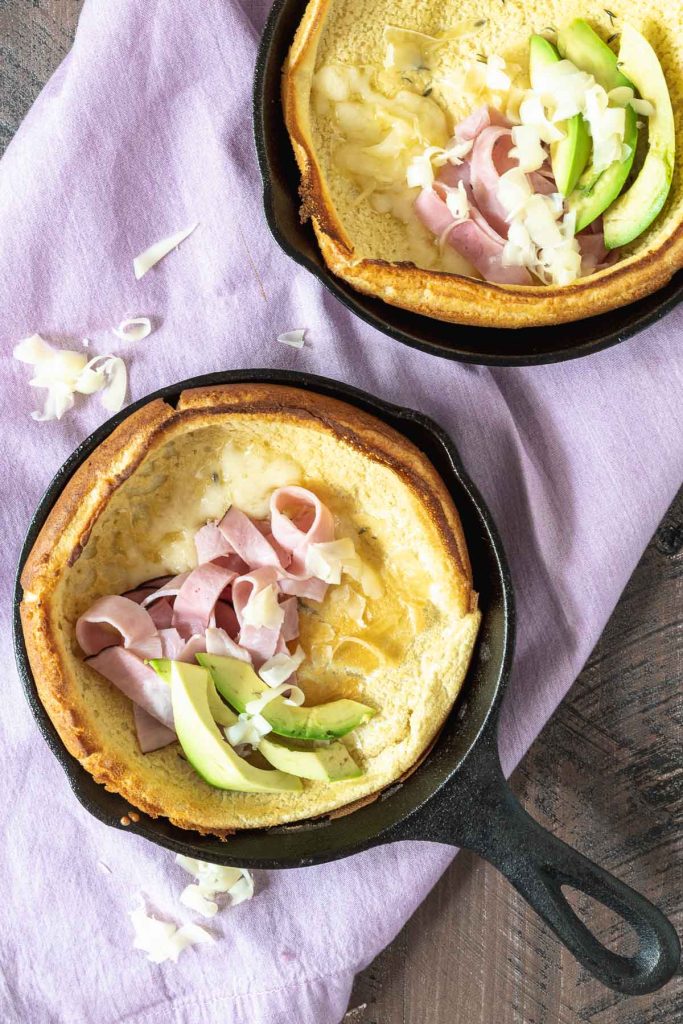 Two mini dutch baby pancakes in cast iron skillets topped with avocado and sliced ham