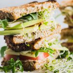 Stacked veggie sandwich with hummus, avocado, tomato & cheese