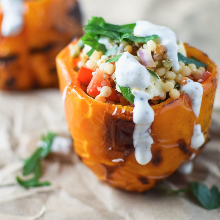 Close up of orange pepper stuffed with couscous and veggies and drizzled with yogurt sauce