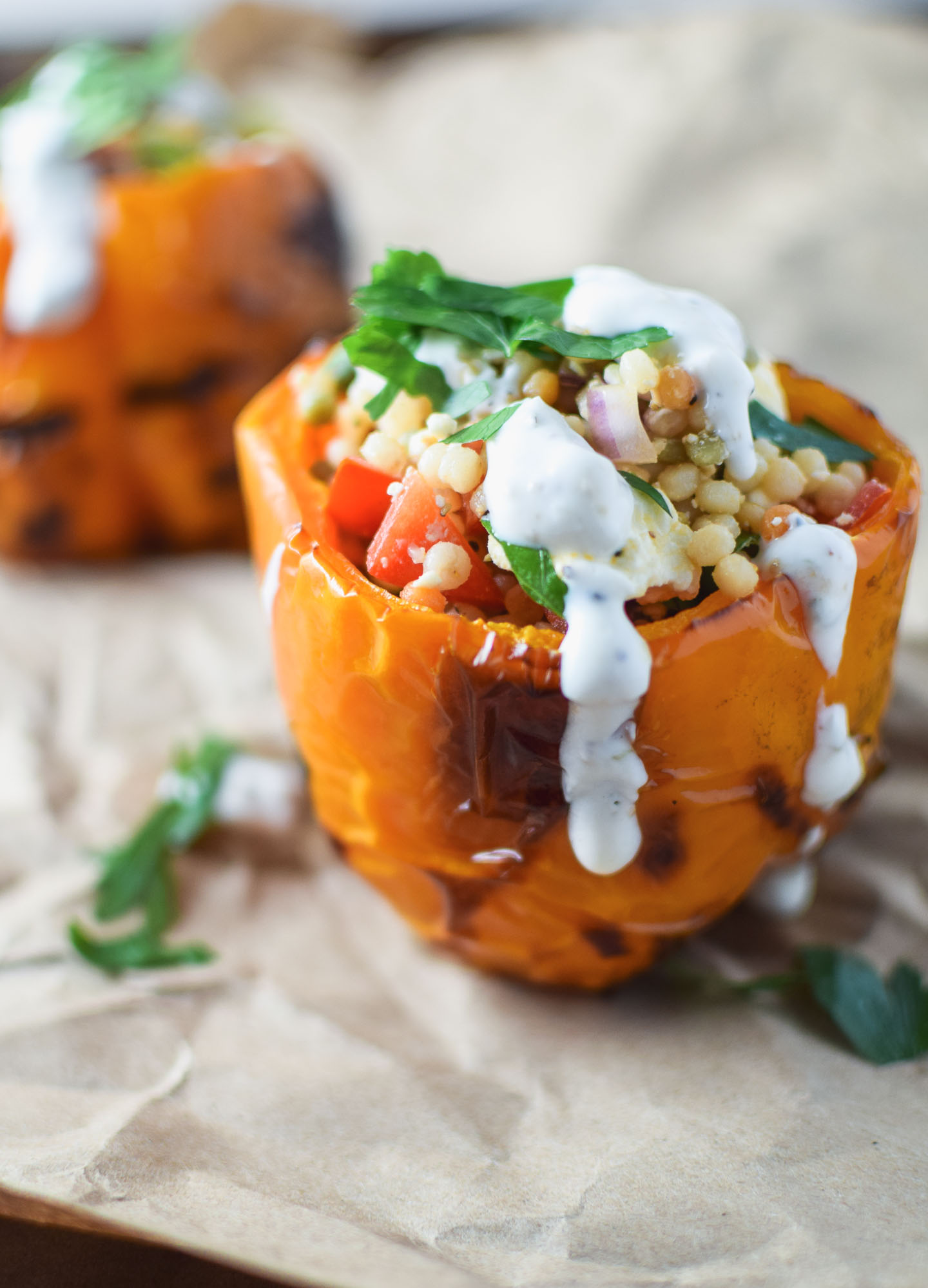 Close up of orange pepper stuffed with couscous and veggies and drizzled with yogurt sauce