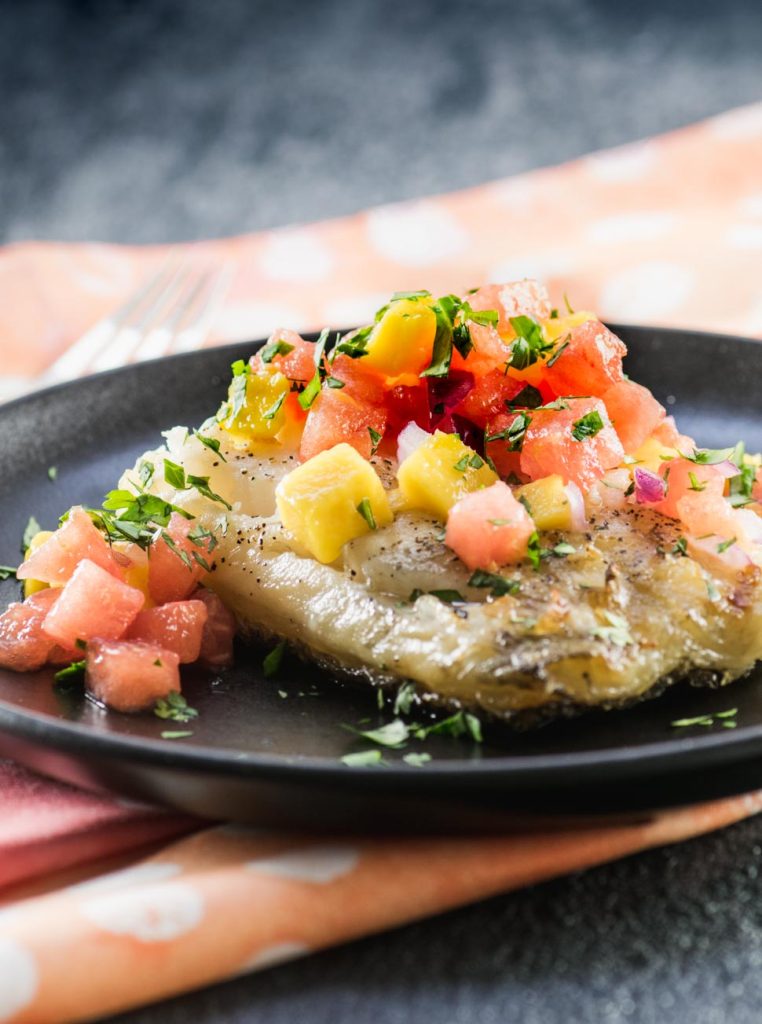 Grilled sea bass filet topped with watermelon mango salsa on a matte black plate
