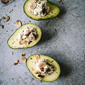 Three avocados stuffed with chicken salad on a light grey background