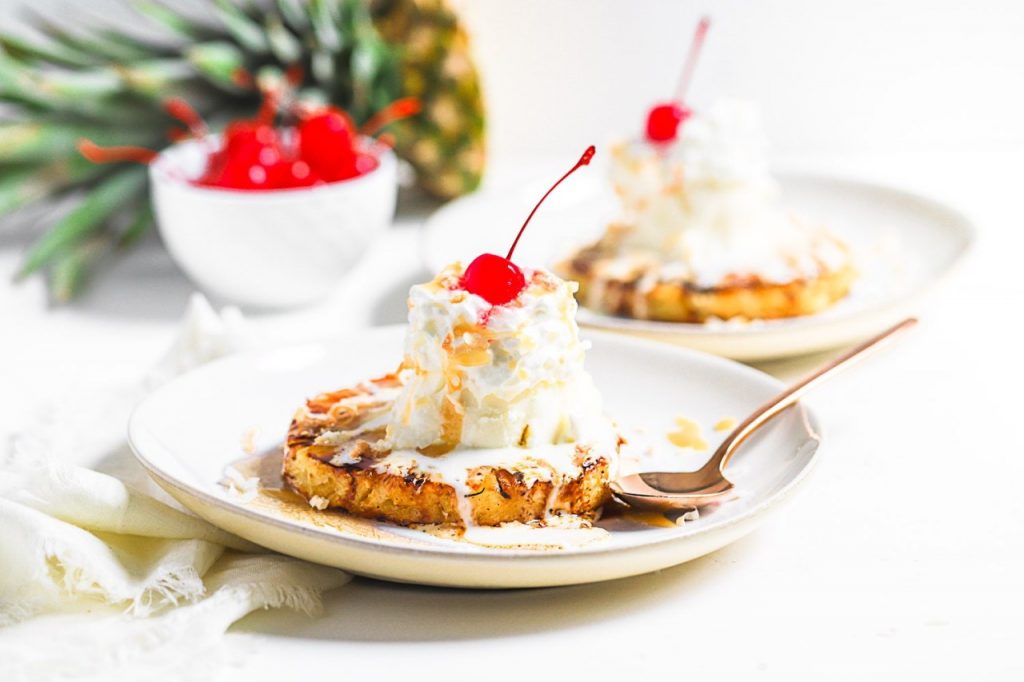 Grilled pineapple slices topped with ice cream and bright red cherries