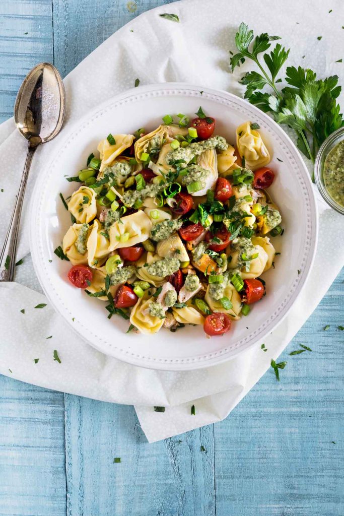 Overhead shot of tortellini pasta salad topped with bright red tomatoes and artichoke hearts