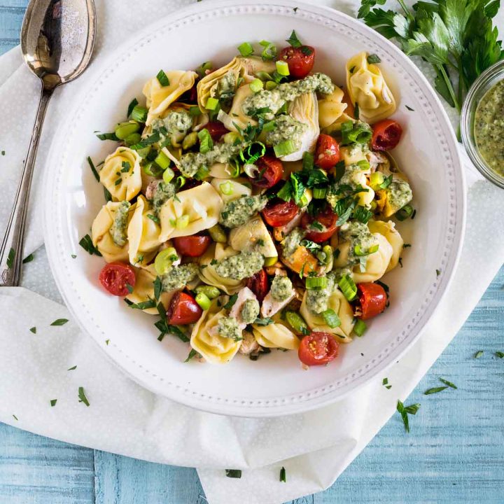 Overhead shot of tortellini pasta salad topped with bright red tomatoes and artichoke hearts