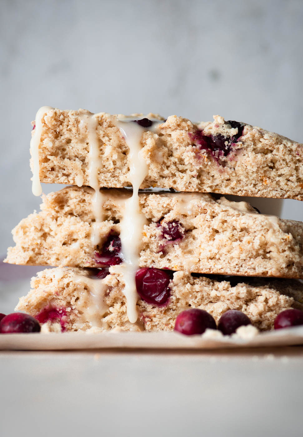 Three cranberry orange scones stacked with glaze dripping down the side