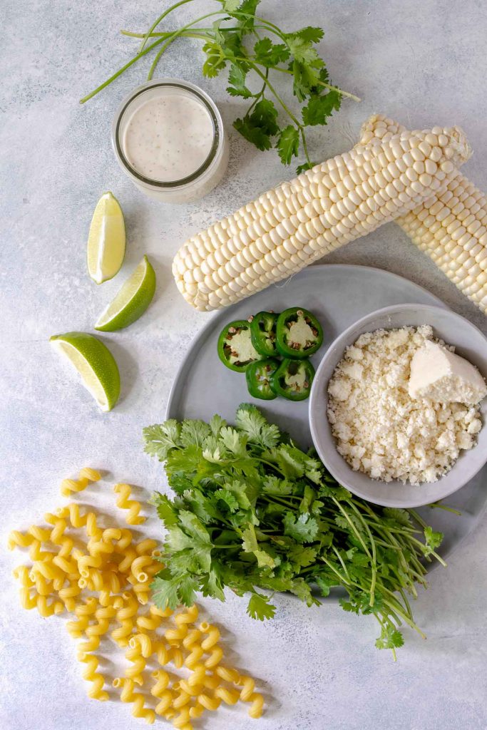 Pasta salad ingredients - corn on the cob, lime wedges, cilantro, dressing and pasta