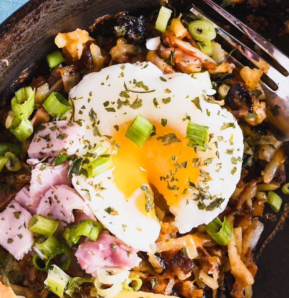 Close up of a poached egg on top of a pan of breakfast hash
