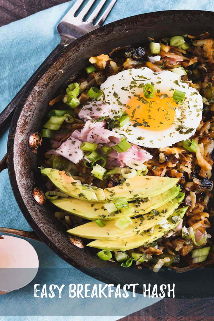 Skillet filled with hash browns, ham, sliced avocado and a poached egg