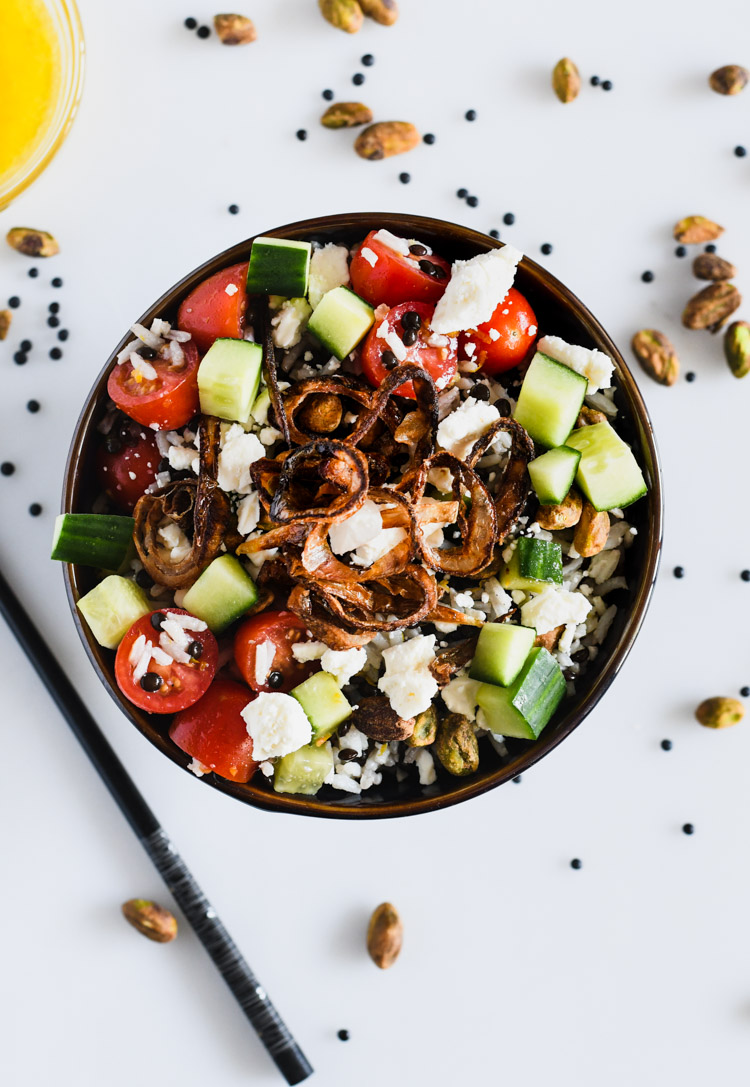 Dark bowl filled with beluga lentil and basmati rice salad topped with crispy shallots and pistachios, chopstick on the side