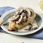 Baked breaded chicken breast on a blue plate topped with a creamy sauce and sliced mushrooms