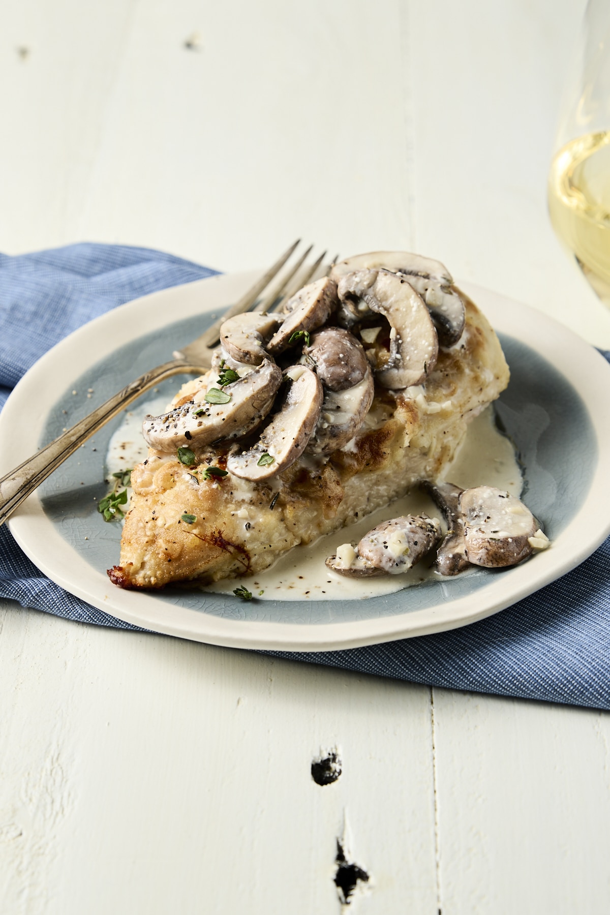 Baked breaded chicken breast on a blue plate topped with a creamy sauce and sliced mushrooms