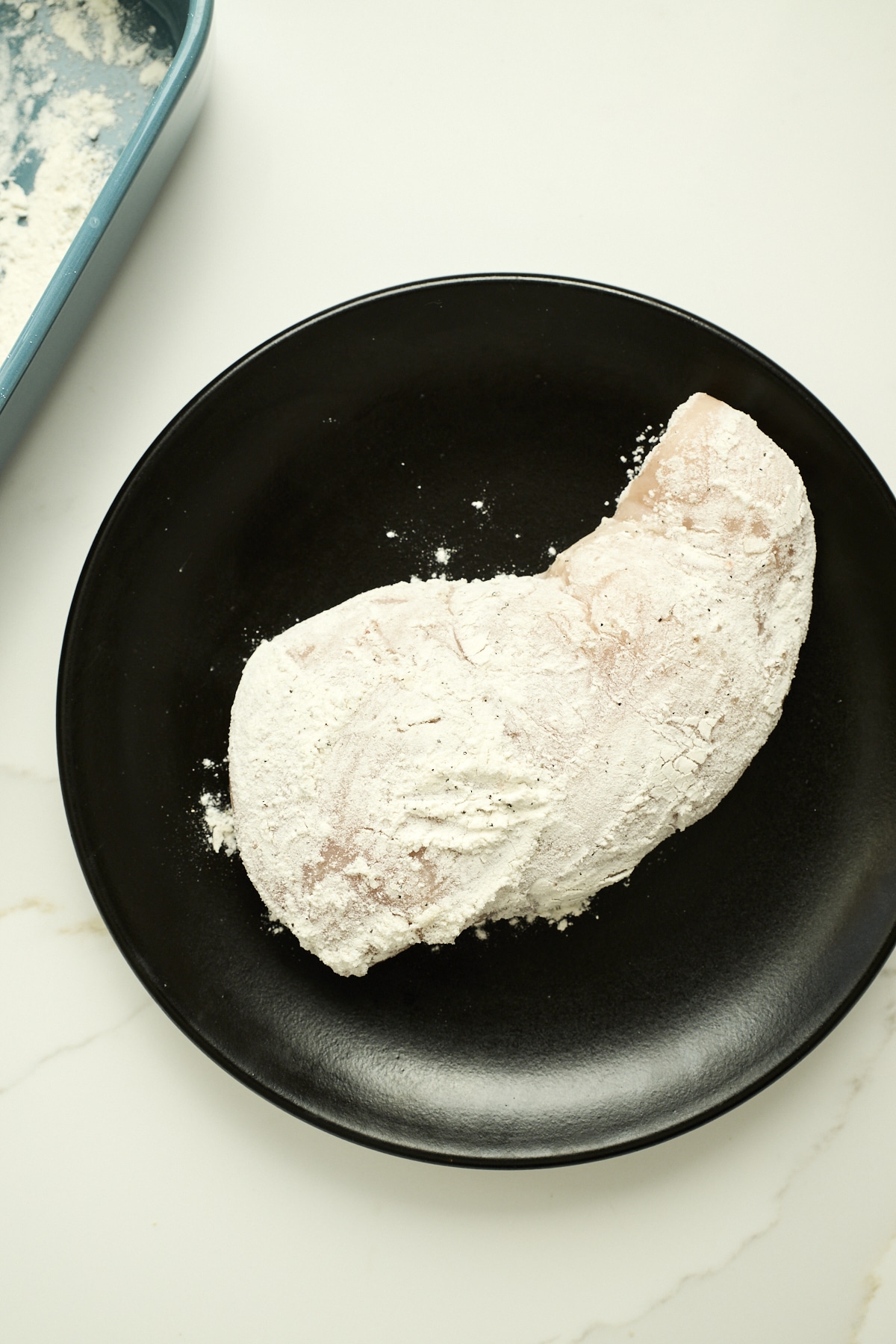 Chicken breast covered in breading flour on a black plate