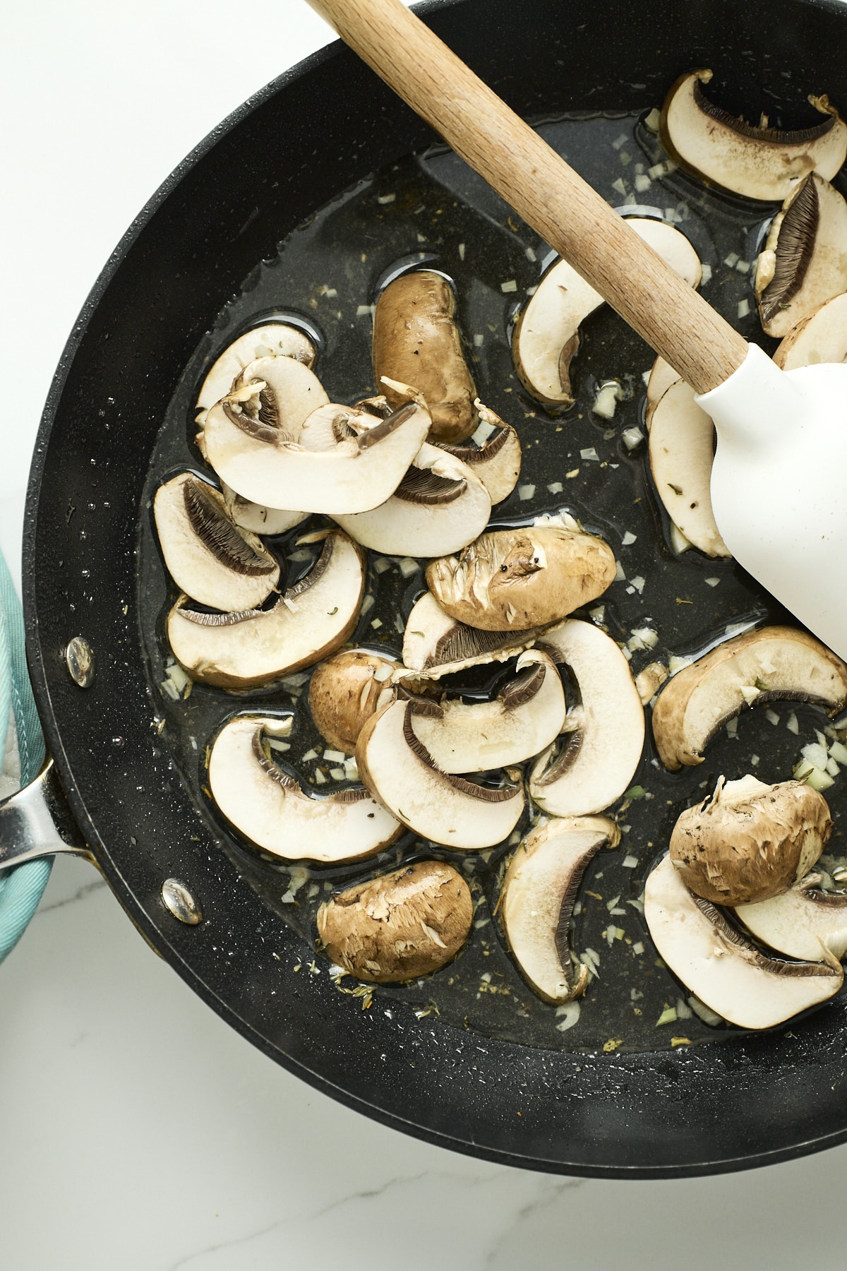 Mushrooms cooking in white wine in a dark pan