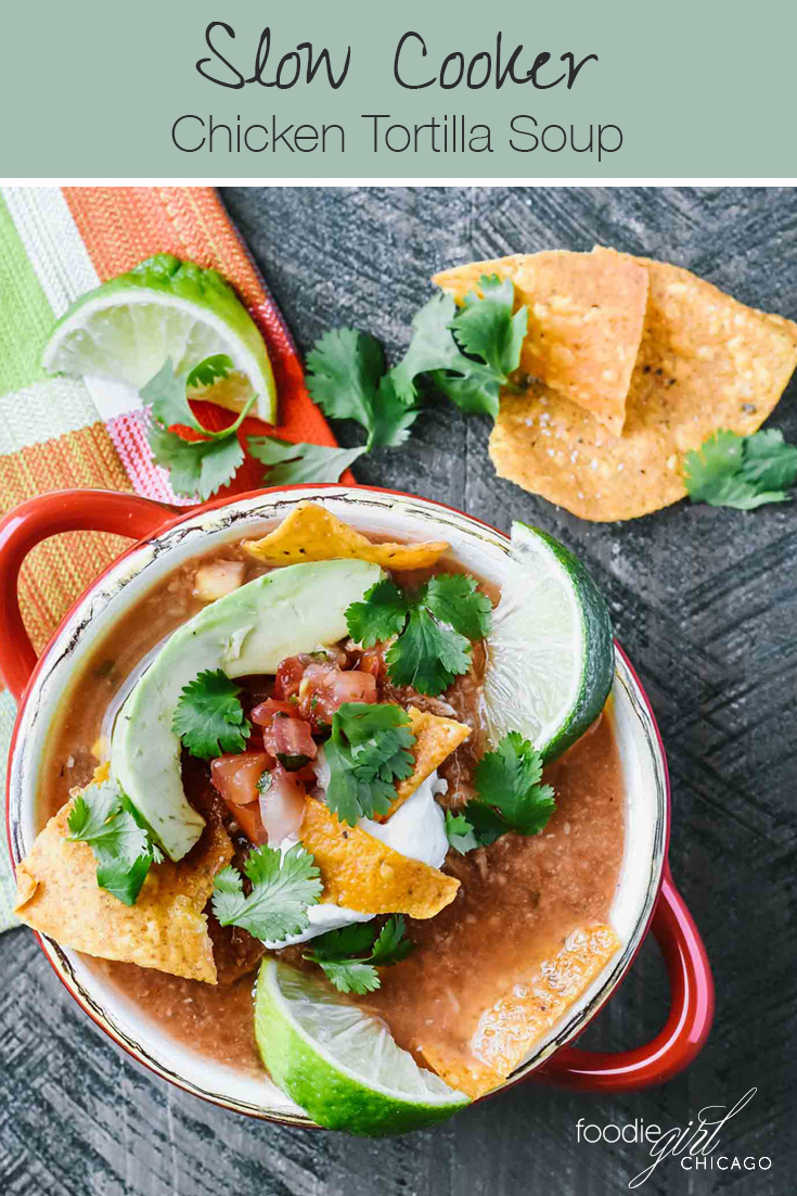 Slow cooker chicken tortilla soup in a red bowl topped with avocado, pico and tortilla chips
