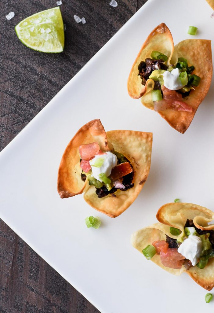 Wonton taco cups from overhead filled with seasoned black beans and topped with guacamole, pico de gallo and cilantro lime sauce