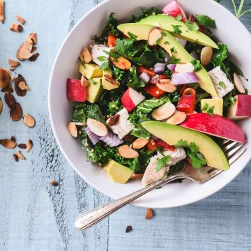 Chopped Kale Salad topped with bright veggies in an off-white bowl