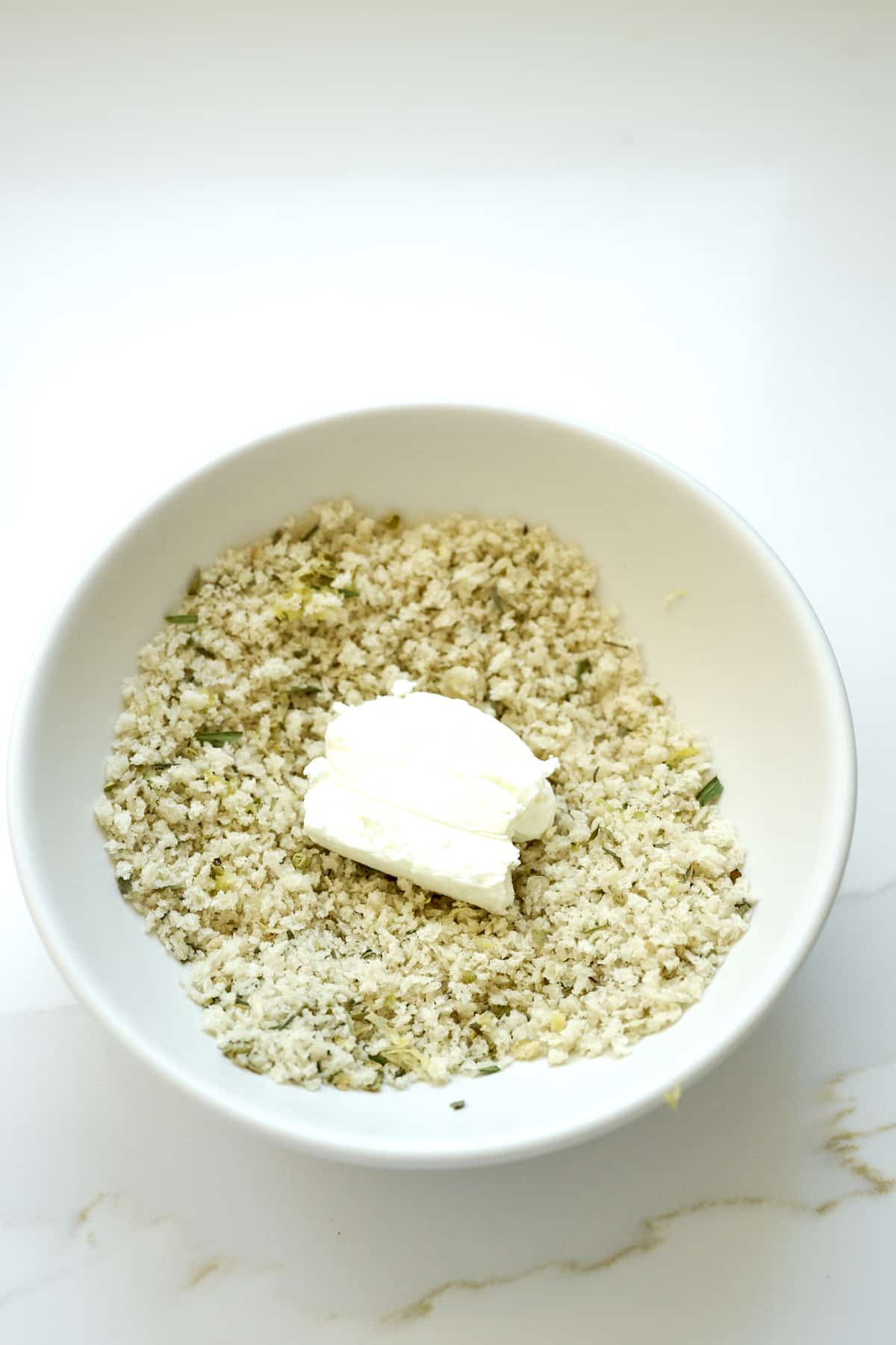 Sliced round of goat cheese being dipped in seasoned Panko breadcrumbs