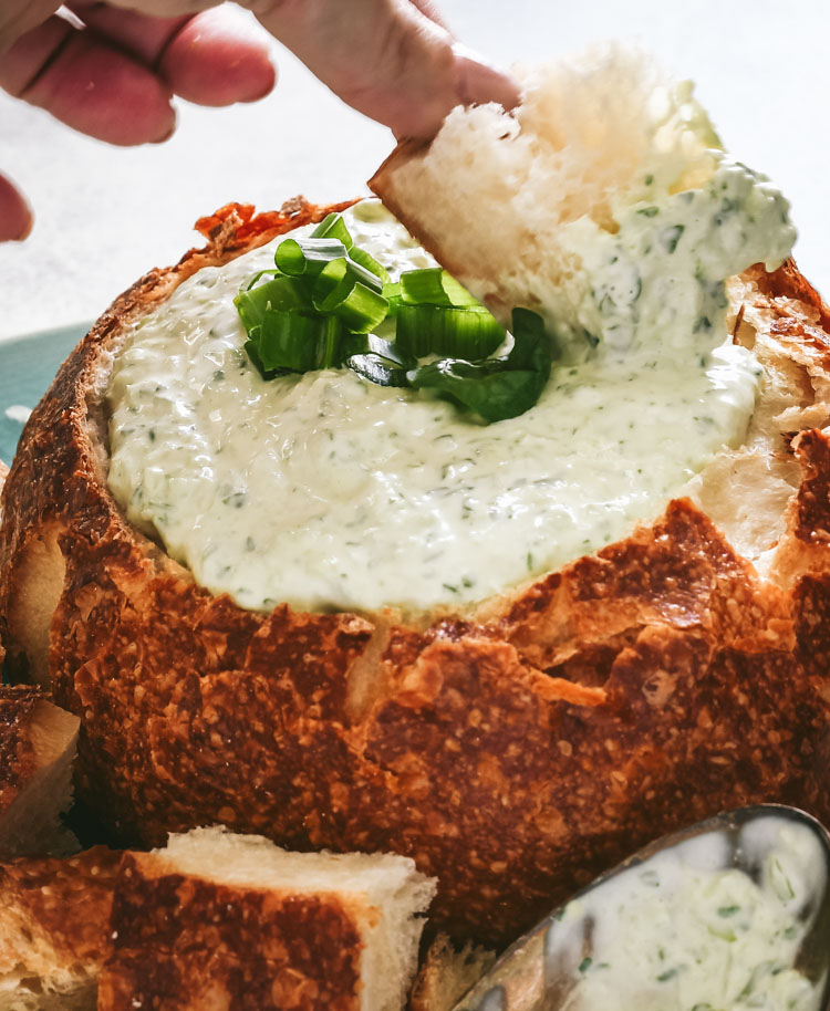 Close up of bread being dipped into spinach dip in a bread bowl