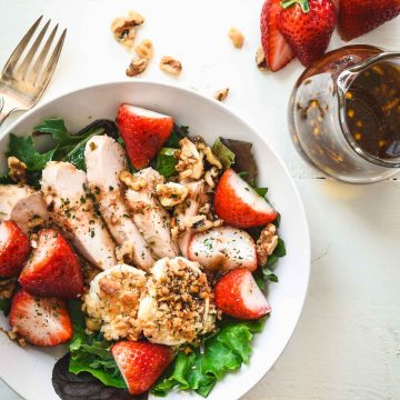 Salad topped with grilled chicken, strawberries and baked goat cheese