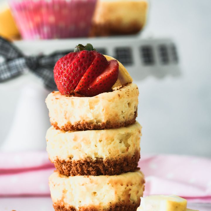 Three mini lemon cheesecakes stacked on top of each other then topped with a sliced strawberry