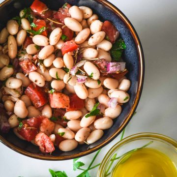 White bean salad with tomatoes and red onions in a dark blue bowl