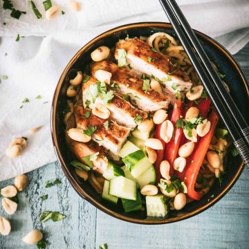 Cold udon noodles in a dark bowl topped with grilled chicken and peanut sauce